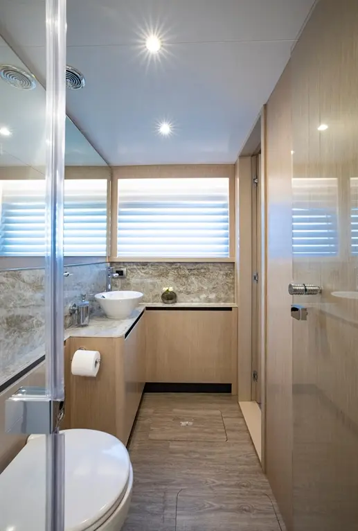 Modern bathroom featuring a white basin, wooden cabinetry, elegant lighting, and grey marble accents.